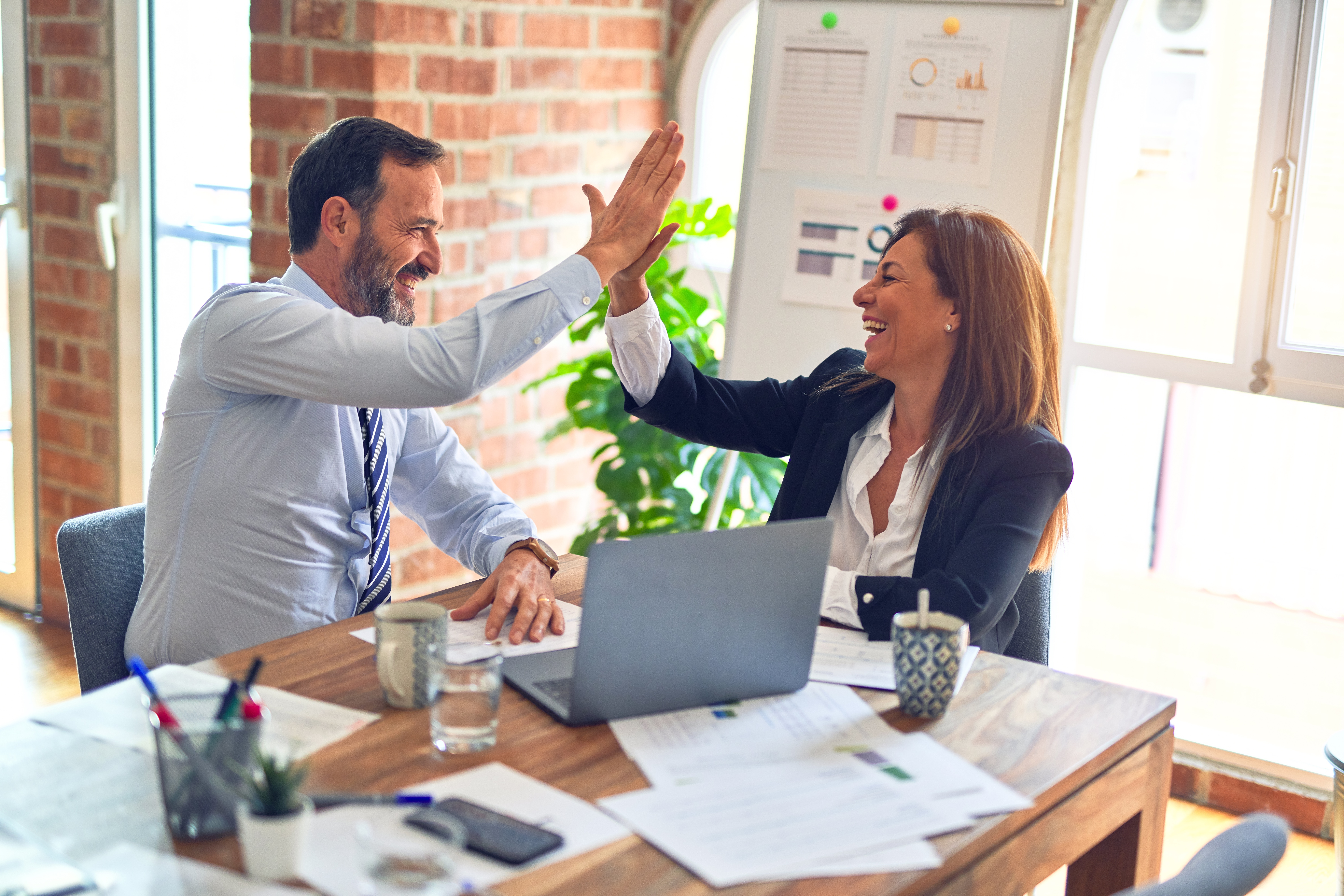 Two people sitting in a business sitting. High five